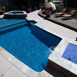 Bright blue pool with attached spa, deck chairs, and umbrella seating