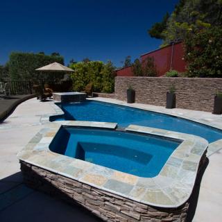Attached spa with stone surround beside a blue backyard pool