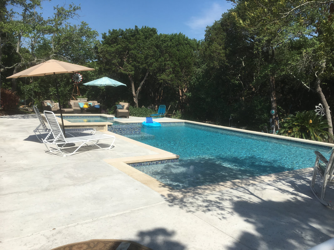 Long backyard pool with patio umbrellas and tree shade